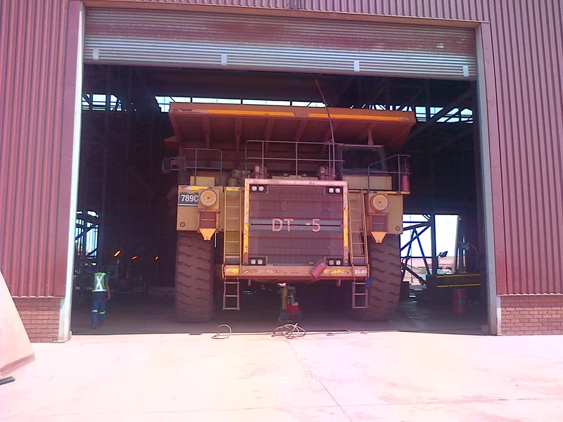 A mining haul truck driving through a giant industrial roller shutter door built by 3 Kings Fabrication